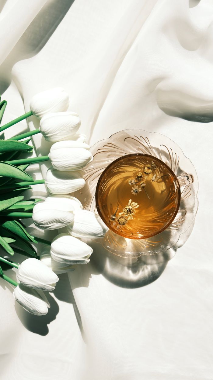 services-01 Aesthetic floral tea in glass cup with white tulips on soft fabric in bright light.